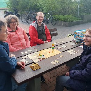 Teilnehmende spielen draußen am Tisch ein Gesellschaftsspiel.
