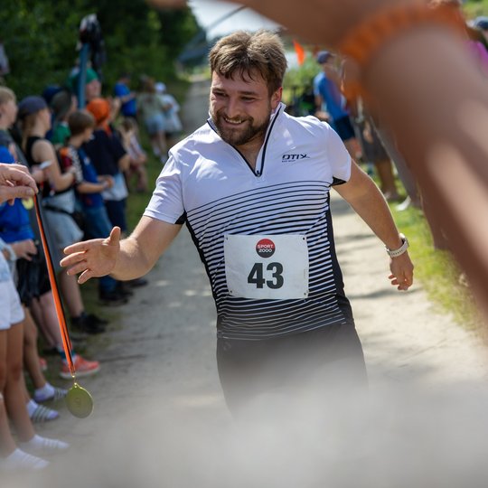 Ein Teilnehmer läuft ins Ziel und greift nach einer Medaille.