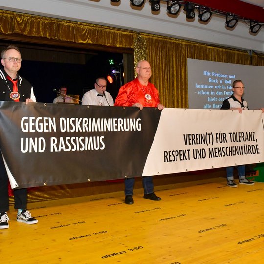 Kolping-Vorsitzender Heiner Placke, KKC-Präsident Heinz Grünebaum und Michael Lührmann präsentieren das Banner für Toleranz, Respekt und Menschenwürde, während Sitzungspräsident Ansgar Speer eine Erklärung gegen Diskriminierung und Rassismus verliest.